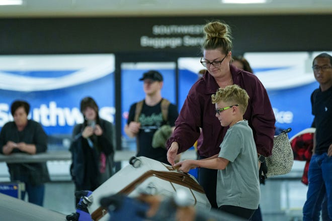 Daniel Miller and son, Weston Miller, 8, pick up a bag from baggage claim as they return home from a Thanksgiving vacation Nov. 26, 2023, at the Phoenix Sky Harbor International Airport in Phoenix.