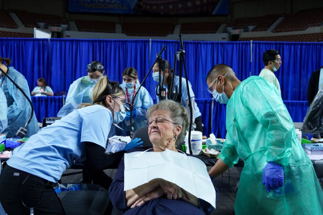 Dr. Margaret Tran (left) and dental assistant, Rojelio Favela (middle) recline Darlene Layton's chair as Darlene sits to receive a filling during the Arizona Dental Mission of Mercy at the Veterans Memorial Coliseum at the Arizona State Fairgrounds on Dec. 8, 2023, in Phoenix. Fillings, among other dental care, are provided free of charge at this annual event.